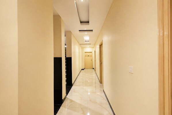 A hotel hallway with a marble floor, light-colored walls, and a ceiling with recessed lighting.