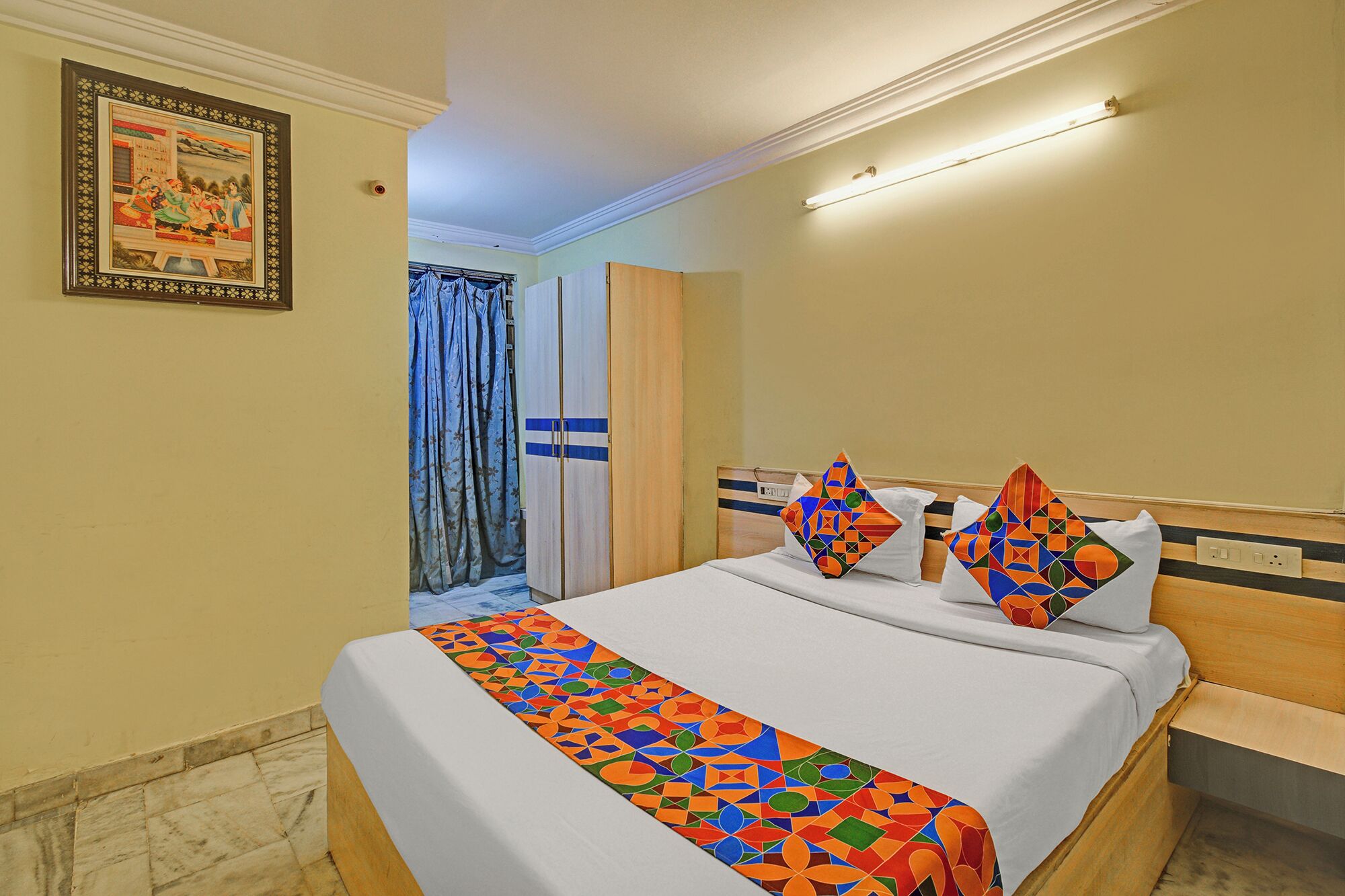 Une chambre d’hôtel avec un lit, une porte, un luminaire et un tableau accroché au mur.