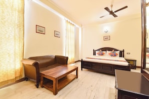 A bedroom with a bed, a wooden table, a sofa, and a ceiling fan. - FabHotel Jd Four Boutique (Jaipur)