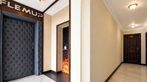 A hallway with a tufted dark-colored headboard, a framed picture of a fire, and a door with a sign above it. - Fabhotel Jd Four Boutique (Jaipur)