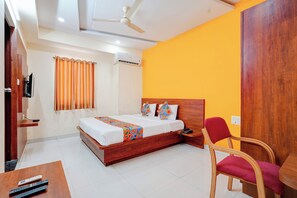 A hotel room with a bed, a chair, a desk, a ceiling fan, and an air conditioning unit. - Fabhotel Silver House Inn (Bangalore)