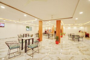 Eine großzügige Hotelhalle mit Marmorböden, mehreren Esstischen mit Stühlen, Deckenventilatoren und topfpflanzen.