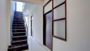 Un couloir avec un escalier en marbre, une porte portant un numéro et une fenêtre.