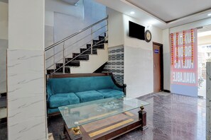 A lobby with a staircase, a sofa, a glass coffee table, and a wall-mounted TV. - Via Metro Inn (Noida)