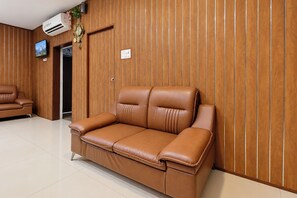 A brown leather sofa against a wooden paneled wall with a television and a clock. - FabHotel La Banian (Indore)