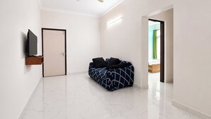 A spacious room with a ceiling fan, a bed, a TV, and a door leading to another room. - Via Dazling Studio (Pune)