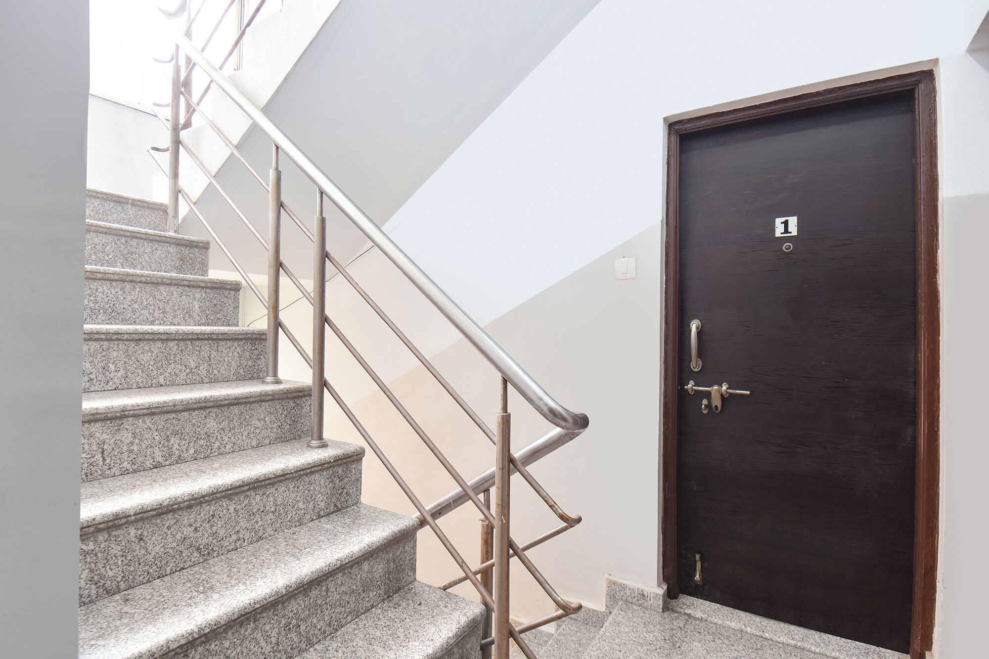 A staircase with metal railings leading to a dark wooden door marked with the number 1.