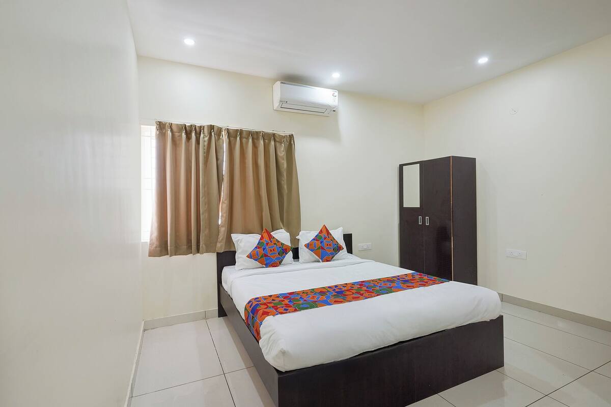 A bedroom with a bed, a wardrobe, a window with curtains, and an air conditioning unit.