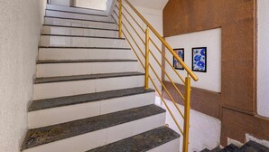 Un escalier avec une rampe jaune, des murs blancs et des œuvres d’art accrochées au mur.