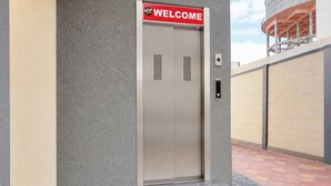 Un ascenseur métallique avec une pancarte indiquant « BIENVENUE », un bouton d’appel et un mur à texture.