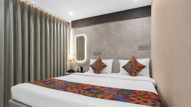 Une chambre d’hôtel avec un lit, des rideaux, une table de chevet, une lampe et un luminaire fixé au mur.