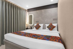 Habitación de hotel con cama, cortinas, mesita de noche, lámpara y aplique de pared.