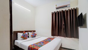 Habitación de hotel con cama, almohadas, colcha estampada, ventana con cortinas, unidad de aire acondicionado y televisor de pantalla plana montado en la pared.