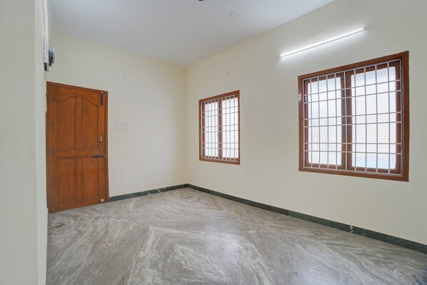 A hallway with a wooden door, a barred window, and a tiled floor. - Fabhotel Nimalan Residency (Chennai)