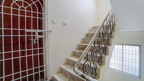 Un escalier avec une rampe en métal, une porte en bois avec une grille en métal et une fenêtre avec une grille en métal.