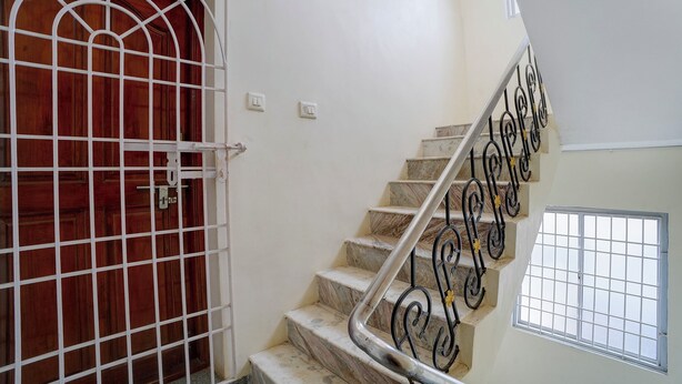 Una escalera con barandilla metálica, una puerta de madera con celosía de metal y una ventana con celosía de metal.