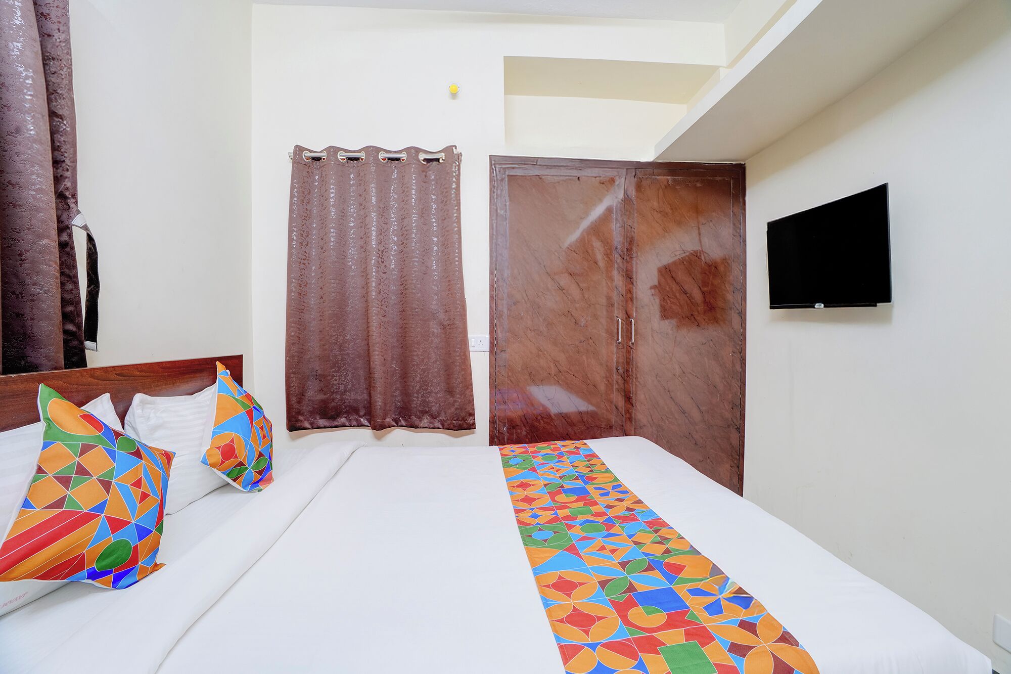 A bedroom with a bed, curtains, a TV, and a wardrobe.