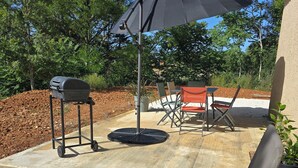 Un patio exterior con una parrilla, una mesa con sillas y un paraguas grande.
