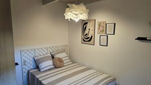Un dormitorio con cama, cabecera, lámpara colgante y cuadros en la pared.