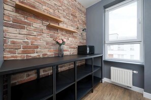Een kamer met een bakstenen muur, een raam, een radiator en een zwarte plankkast.