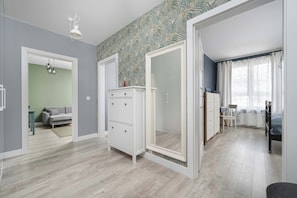 A room with a wooden floor, a white wardrobe, a grey sofa, and a bed with a blue bedspread.