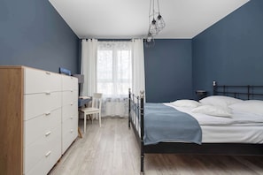 A bedroom with a bed, dresser, chair, and window with curtains.
