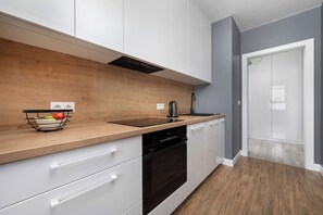 Une cuisine moderne avec des meubles blancs, un plan de travail en bois, un four noir et une bouilloire.