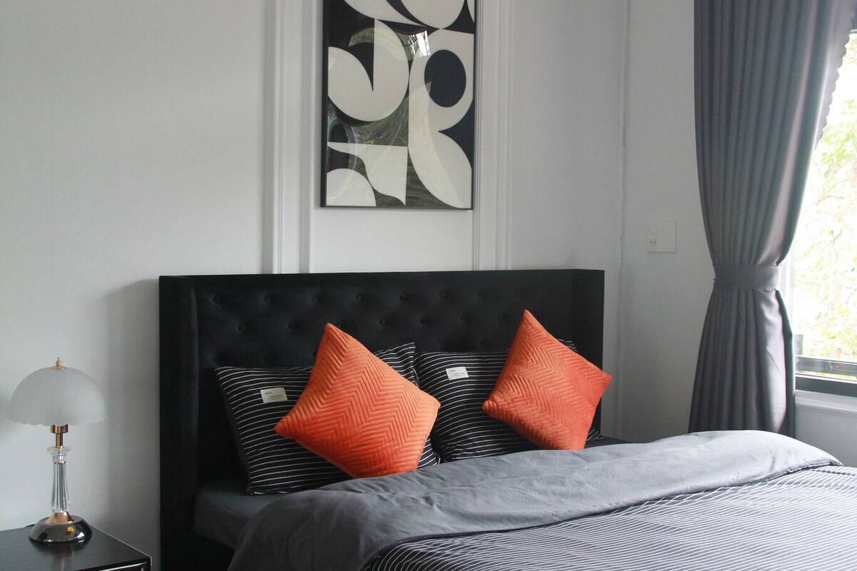 A modern bedroom with a large bed, a nightstand, a lamp, and a framed abstract artwork on the wall.
