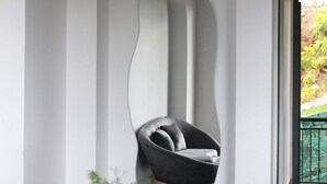 A modern interior with a curved wall, a black leather chair, a glass vase with greenery, and a black and gold table. - Thai Bao Chau 3  (Xuan Huong - Da Lat)
