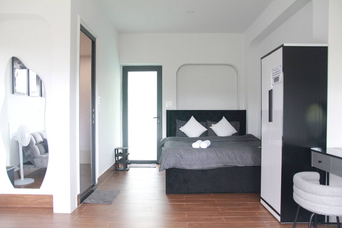 A modern bedroom with a bed, a desk, and a refrigerator.