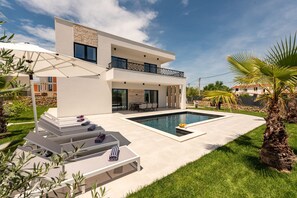 Ein modernes, zweistöckiges Haus mit Swimmingpool, Sitzgelegenheiten im Freien und einem gepflegten Rasen.