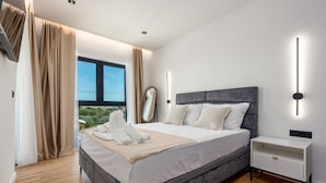 A modern bedroom with a large bed, bedside tables, a mirror, and a view of greenery outside. - Villa Kri to Zadarvillas (Privlaka)