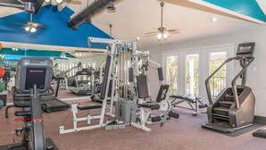 Ett gym med träningsutrustning, takfläktar och stora fönster.
