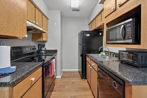 A compact kitchen with wooden cabinets, a black refrigerator, a microwave, a stove, and a sink. - Modern comfort in a 2-bedroom layout (Lubbock)