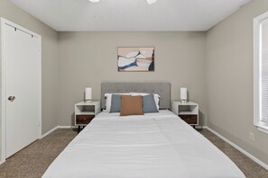 A bedroom with a bed, two bedside tables, a nightstand, a wall-mounted artwork, and a door. - Modern comfort in a 2-bedroom layout (Lubbock)