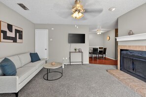 Ein Wohnzimmer mit Sofa, Couchtisch, Kamin, Fernseher und Essbereich.