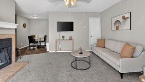 Un salon moderne avec une cheminée, un canapé, une table basse, un téléviseur et un coin repas.