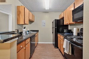 A kitchen with wooden cabinets, a black refrigerator, a stove, and a microwave. - Well-appointed 2BR in prime location (Lubbock)