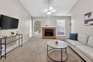 Ein Wohnzimmer mit Kamin, Deckenventilator, Wandfernseher und einer Couch.