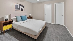 Une chambre à coucher comprenant un lit, des tables de chevet, un ventilateur de plafond et deux portes.
