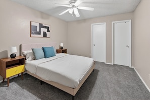 A bedroom with a bed, nightstands, a ceiling fan, and two doors. - Relax in this spacious 2BR apartment (Lubbock)