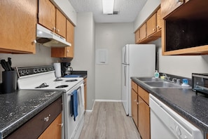 A kitchen with wooden cabinets, a white stove, a refrigerator, and a dishwasher. - Relax in this spacious 2BR apartment (Lubbock)