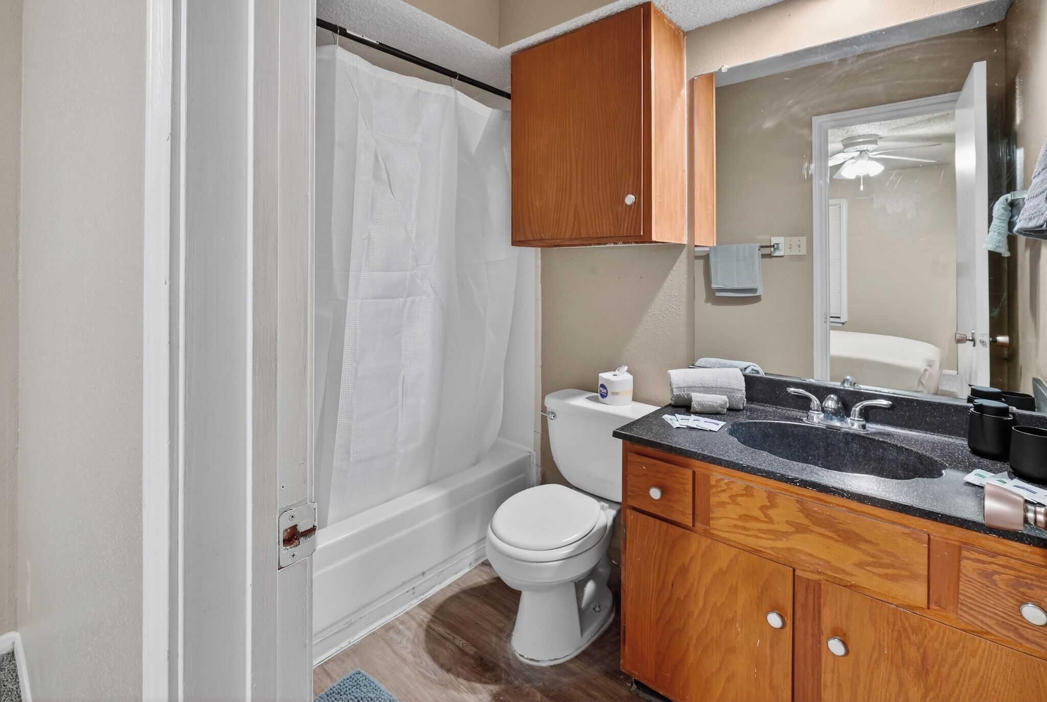A bathroom with a shower, toilet, sink, and wooden cabinets.