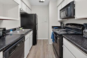 A compact kitchen with a black refrigerator, stove, and microwave. - Updated 2BR with great natural light (Lubbock)
