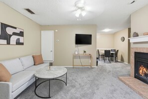Ein Wohnzimmer mit einer Couch, einem runden Couchtisch, einem Fernseher, einem Kamin und einem Essbereich mit Stühlen und einem Tisch.