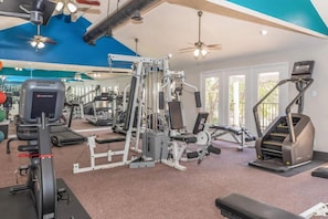Ein Fitnessraum mit Trainingsgeräten, Deckenventilatoren und großen Fenstern.