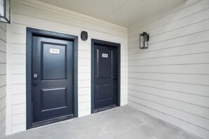Two black doors with numbers 1912 and 1913, white siding, and a concrete walkway. - Stylish 1-bedroom featuring contemporary finishes. (Austin)