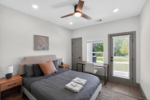 A bedroom with a bed, bedside tables, a desk, a chair, a ceiling fan, and a door leading to a balcony. - Stylish 1-bedroom featuring contemporary finishes. (Austin)