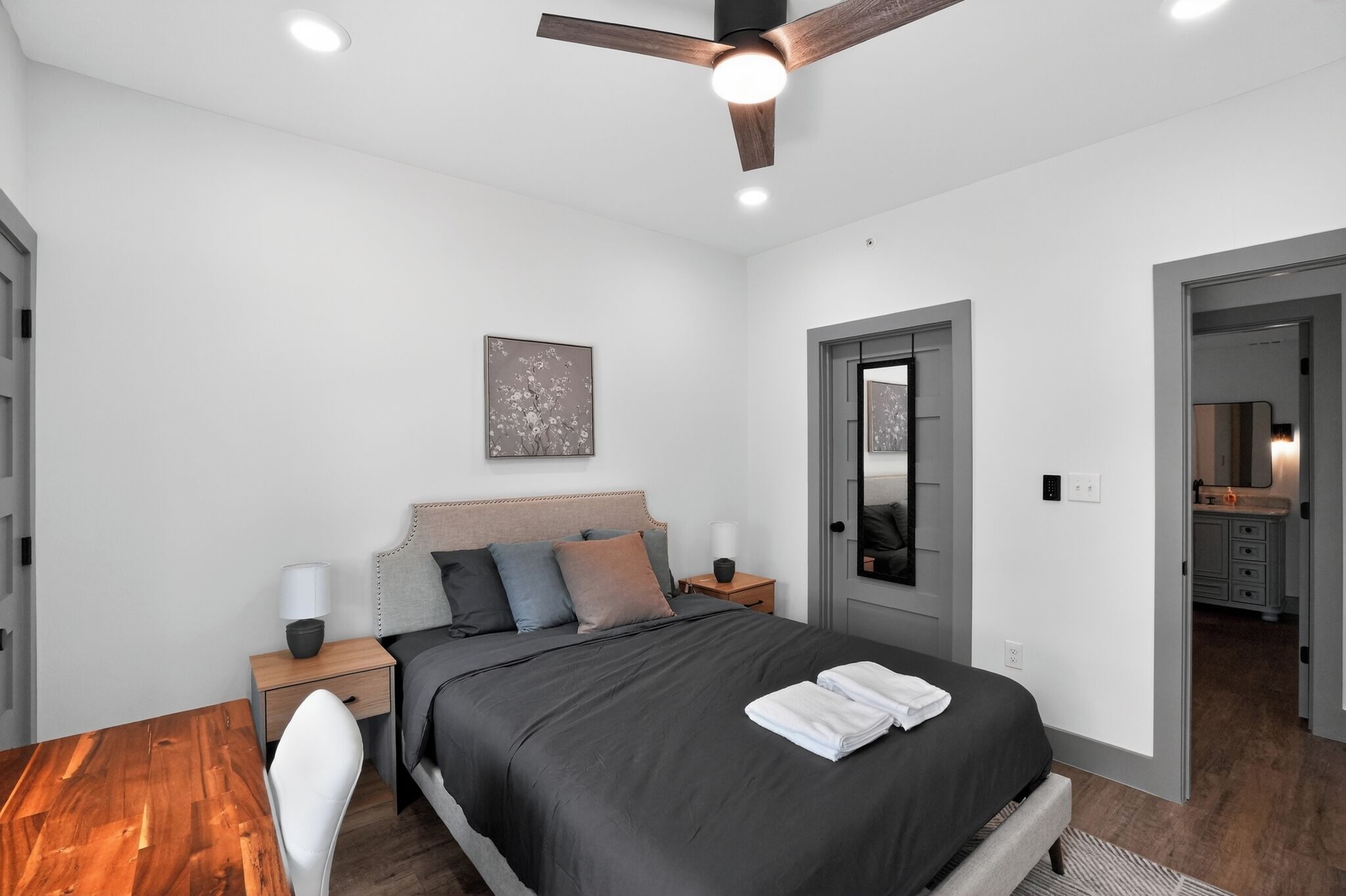 A modern bedroom with a bed, bedside tables, a ceiling fan, and a door leading to a bathroom.