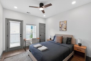 Ein Schlafzimmer mit Bett, Nachttischen, Schreibtisch, Deckenventilator und einem Fenster mit Jalousien.
